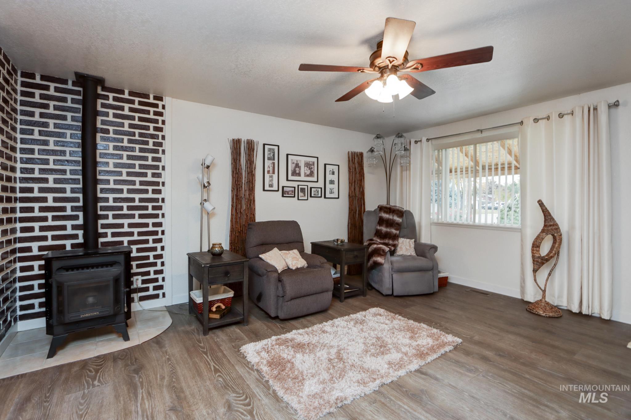 Living area featuring a wood stove, wood finished floors, and a ceiling fan