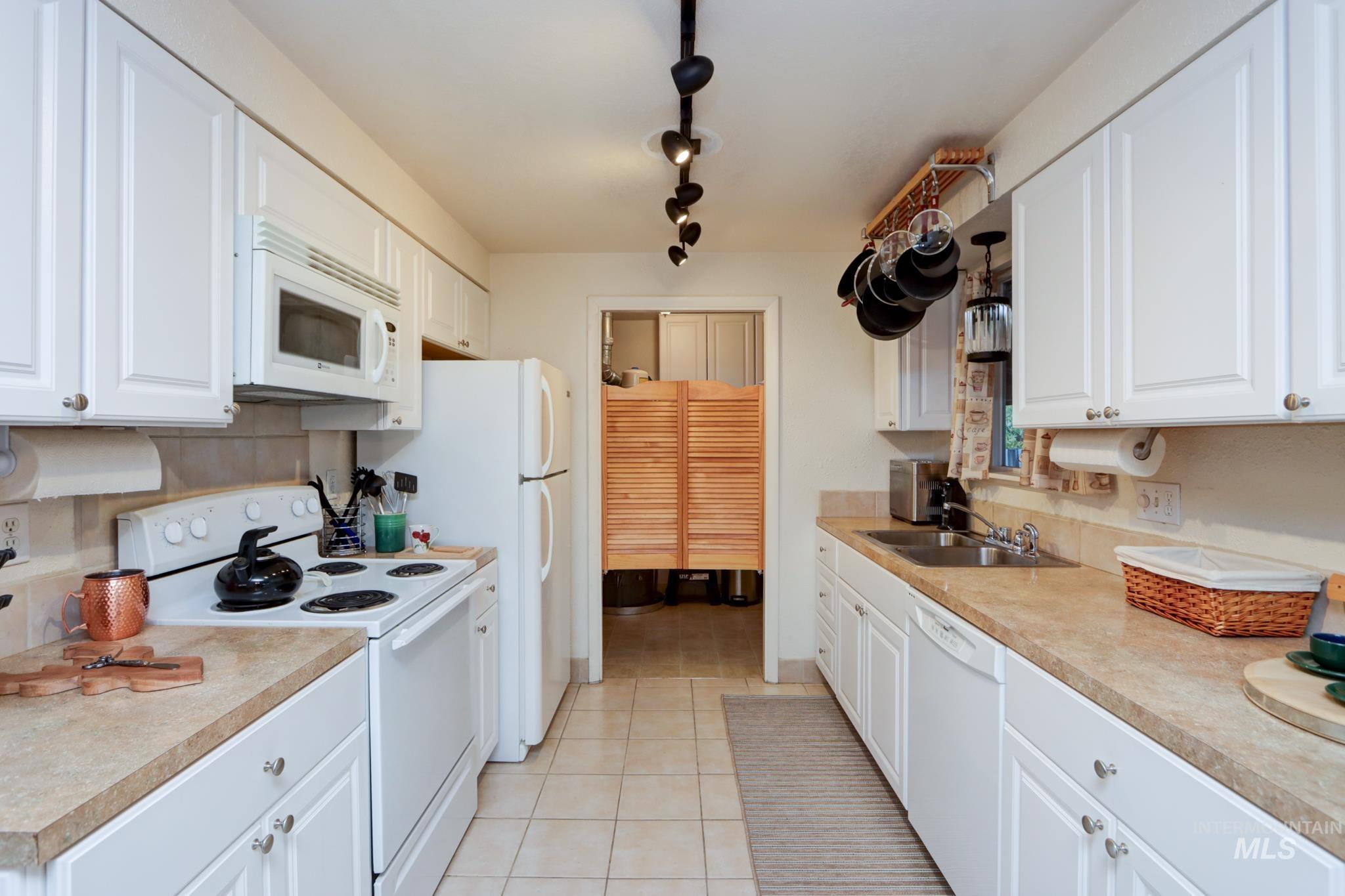 Kitchen featuring white appliances, white cabinetry, light countertops, light tile patterned floors, and rail lighting