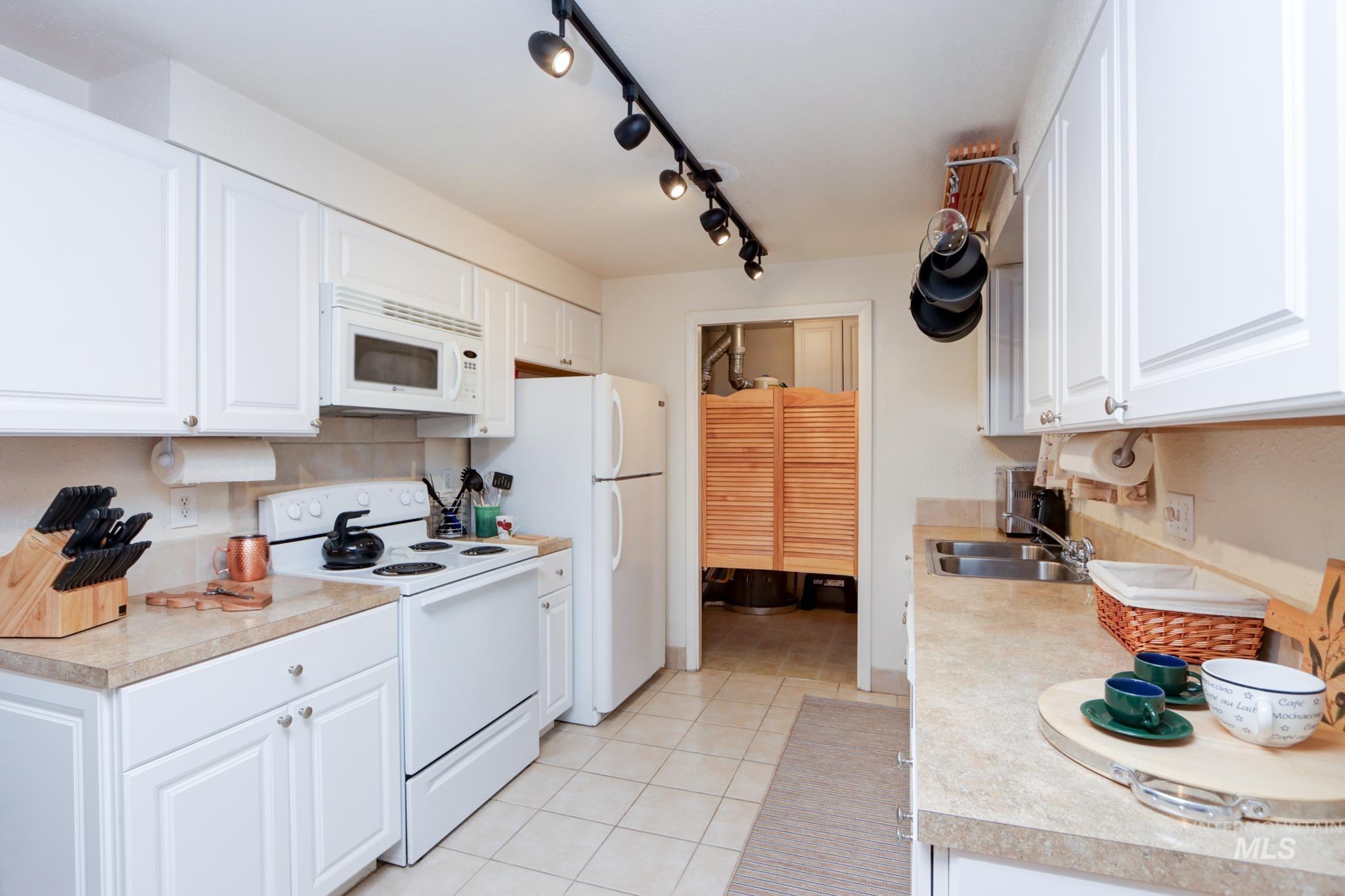 Kitchen featuring white appliances, light countertops, white cabinetry, light tile patterned floors, and tasteful backsplash