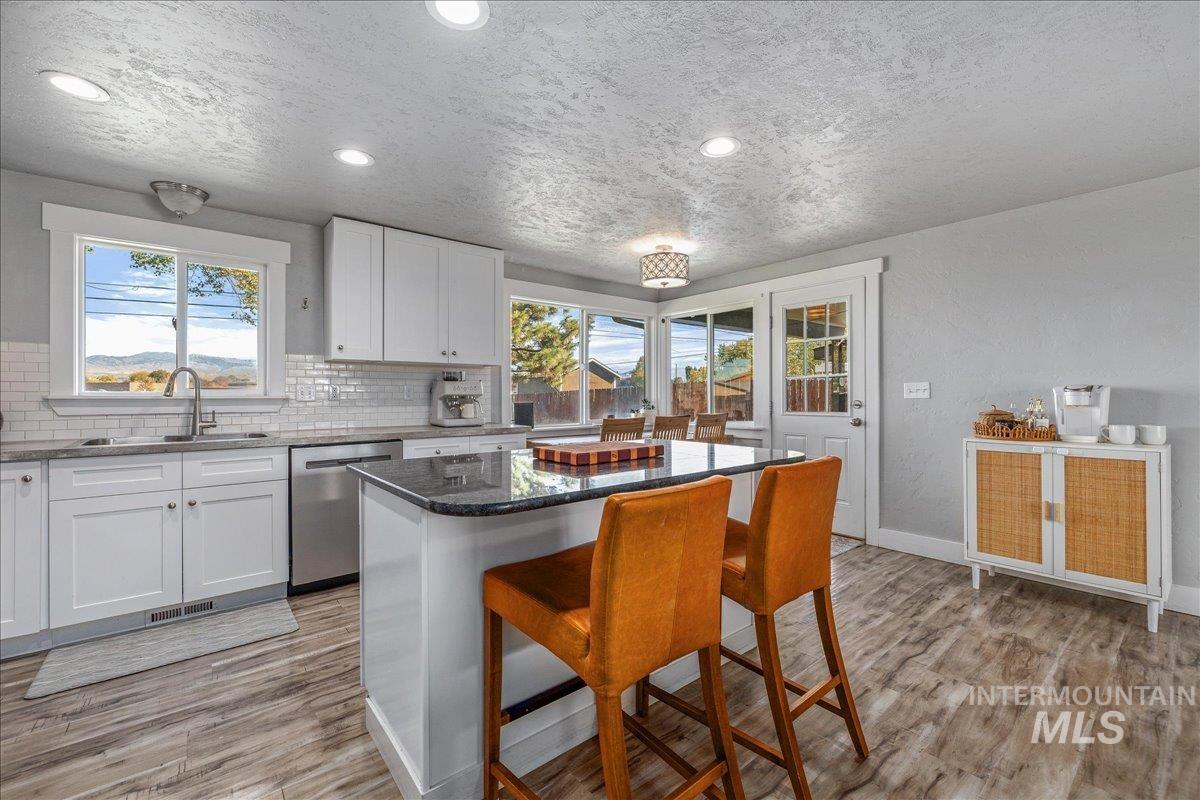 Kitchen featuring dark stone countertops, white cabinets, backsplash, stainless steel dishwasher, and light wood finished floors