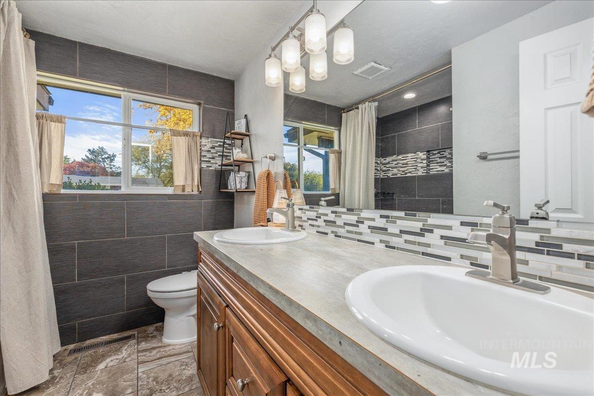 Bathroom featuring tile walls, double vanity, a tile shower, and backsplash