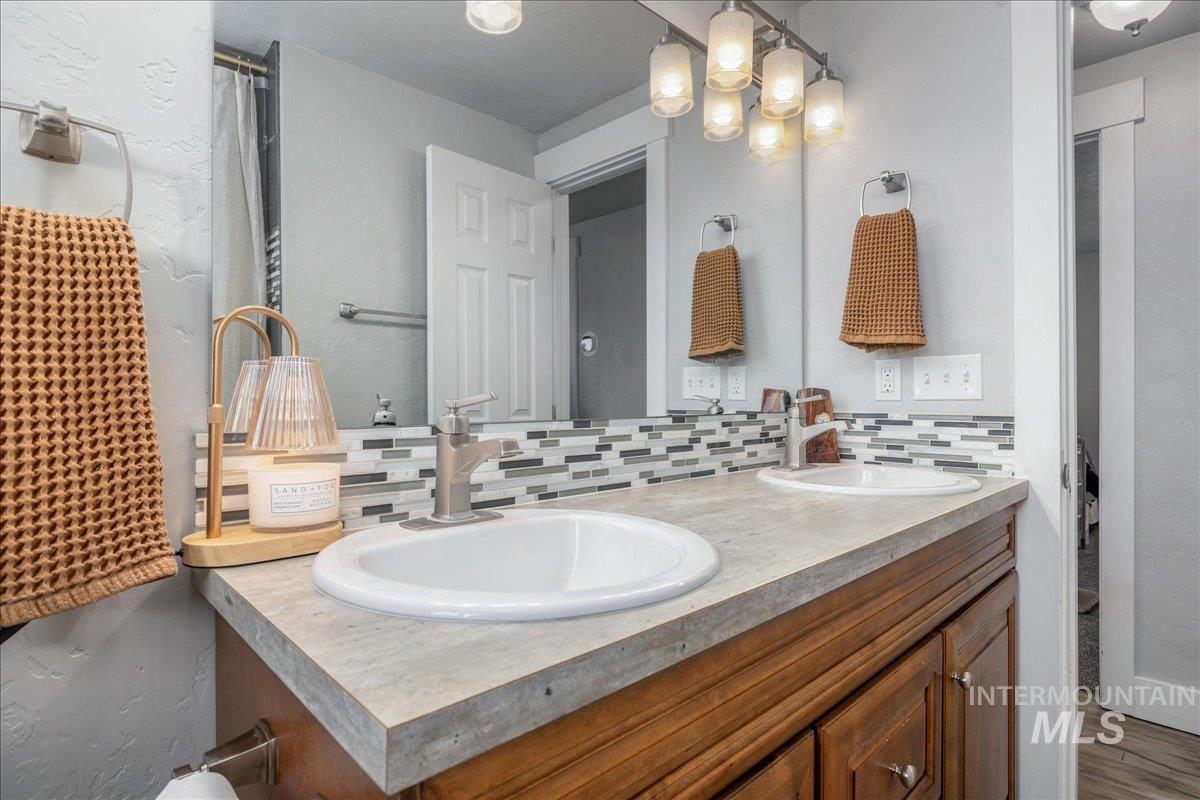 Full bath featuring double vanity, a textured wall, tasteful backsplash, a shower with curtain, and wood finished floors