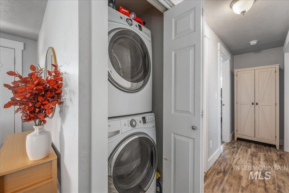 Laundry area with a textured ceiling, wood finished floors, and stacked washing machine and dryer