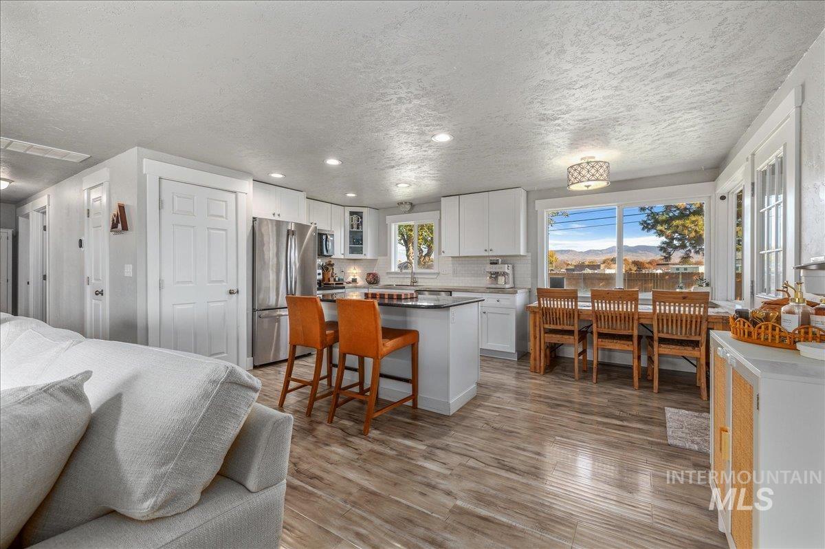 Kitchen with white cabinetry, backsplash, a kitchen island, appliances with stainless steel finishes, and light wood finished floors