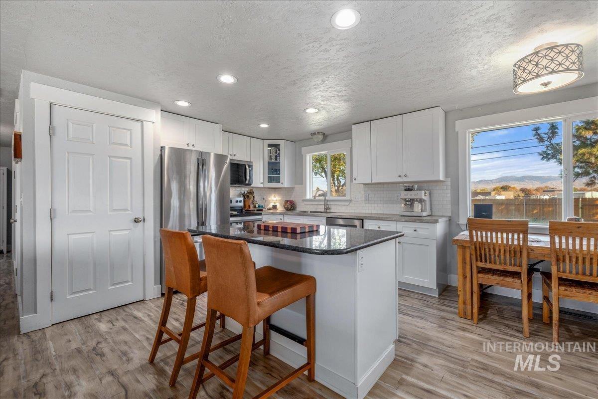 Kitchen with a kitchen breakfast bar, a center island, white cabinetry, dark stone counters, and light wood-style flooring