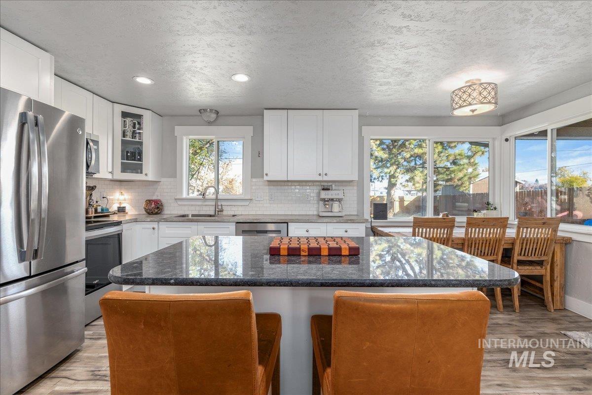 Kitchen featuring stainless steel appliances, dark stone countertops, light wood-type flooring, white cabinets, and glass insert cabinets