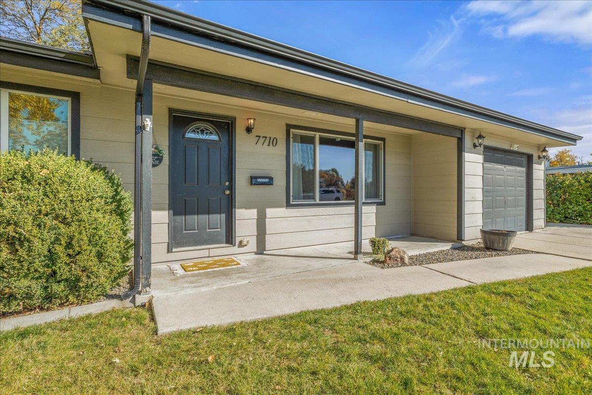 Doorway to property featuring covered porch, an attached garage, and a lawn