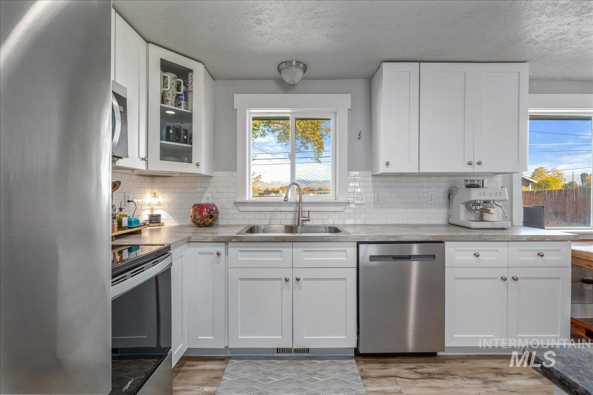 Kitchen featuring appliances with stainless steel finishes, white cabinetry, glass insert cabinets, and a textured ceiling