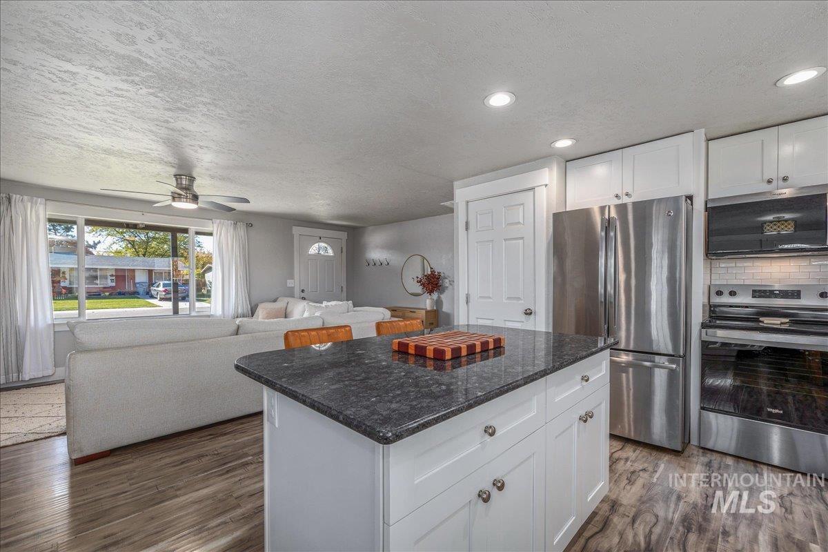 Kitchen featuring stainless steel appliances, white cabinetry, dark stone countertops, open floor plan, and a textured ceiling
