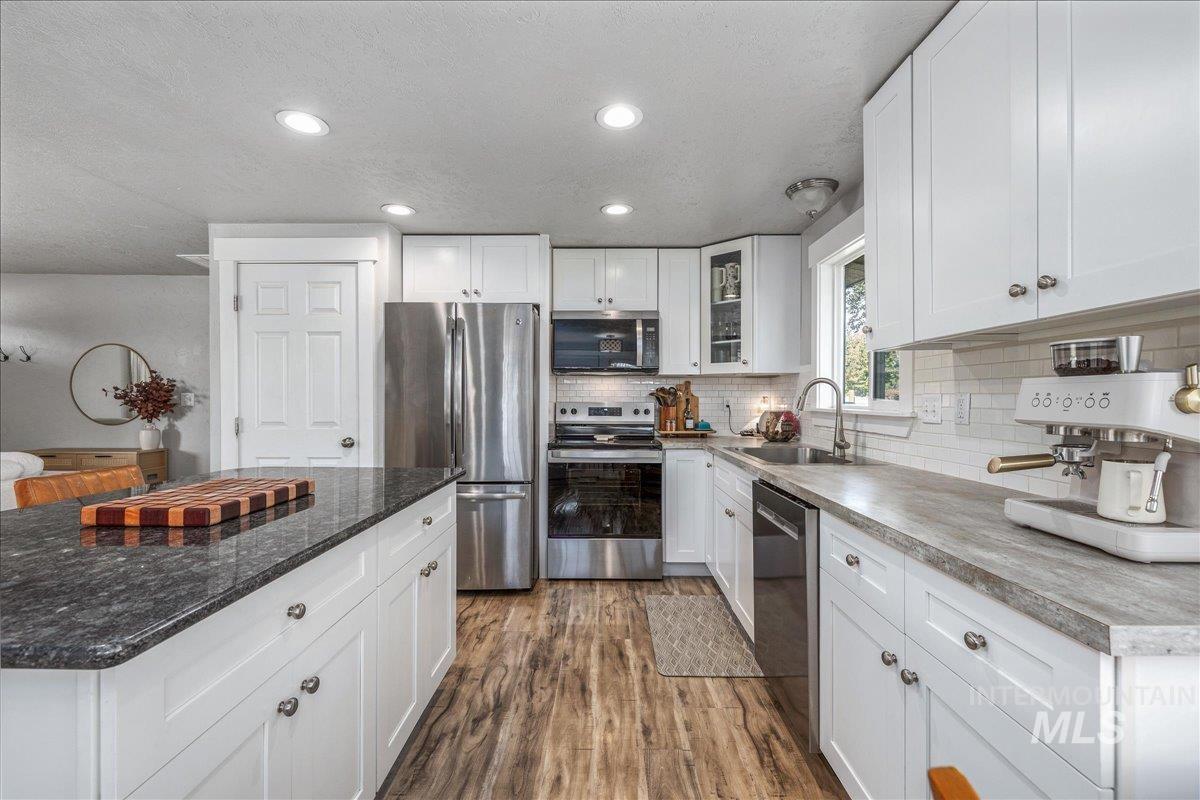 Kitchen with appliances with stainless steel finishes, white cabinetry, dark wood finished floors, recessed lighting, and a textured ceiling