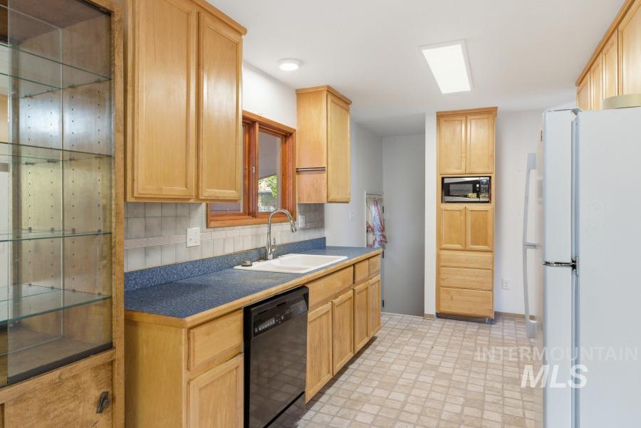 Kitchen with freestanding refrigerator, black dishwasher, decorative backsplash, light brown cabinets, and stainless steel microwave