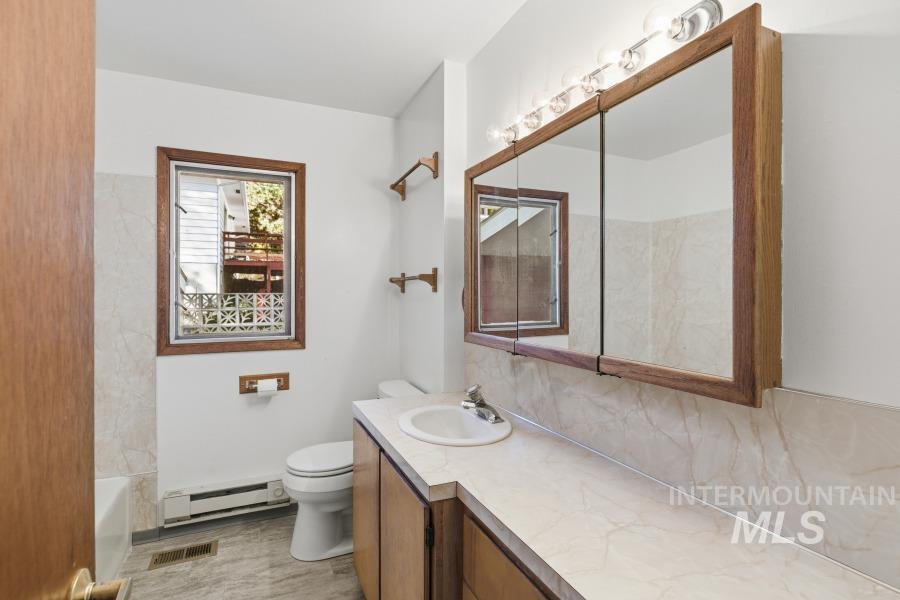 Bathroom with a baseboard radiator, vanity, decorative backsplash, and shower / washtub combination