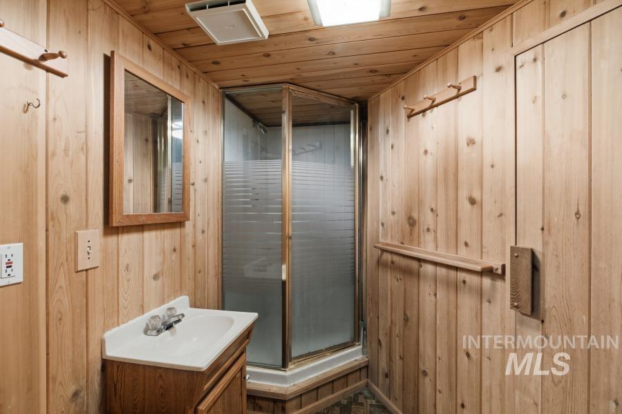 Full bath with wood walls, a stall shower, vanity, wooden ceiling, and a relaxing sauna