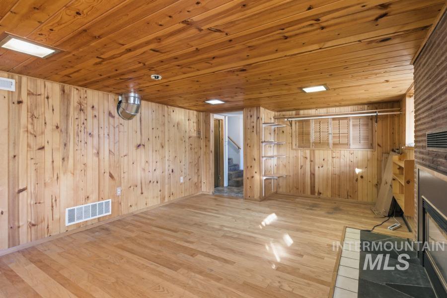 Unfurnished living room with stairway, wooden ceiling, light wood-style flooring, a glass covered fireplace, and wood walls