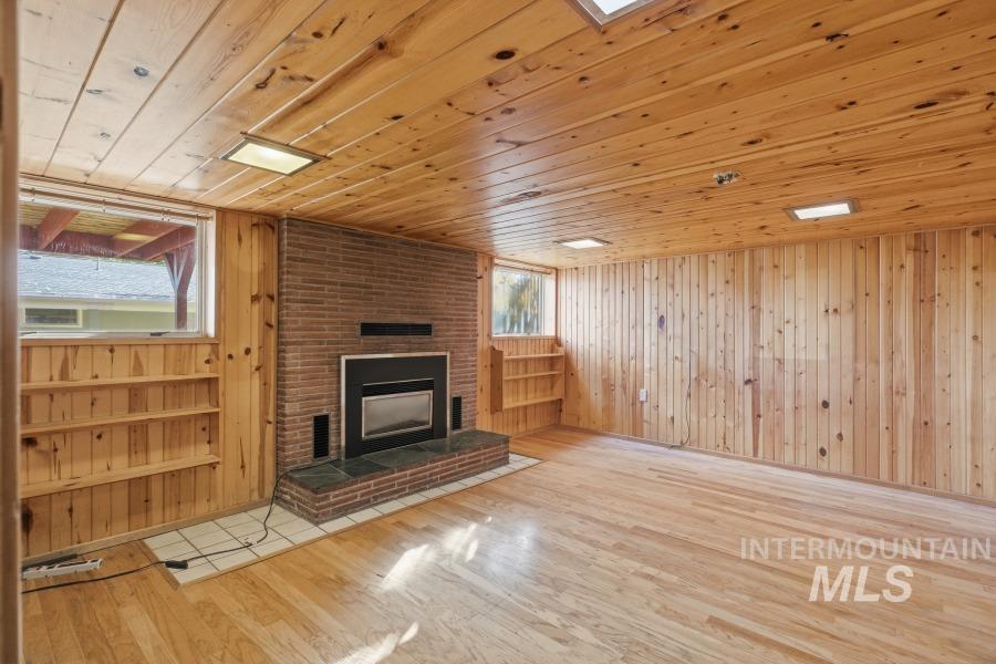 Unfurnished living room featuring wood walls, wood ceiling, light wood-type flooring, and a fireplace