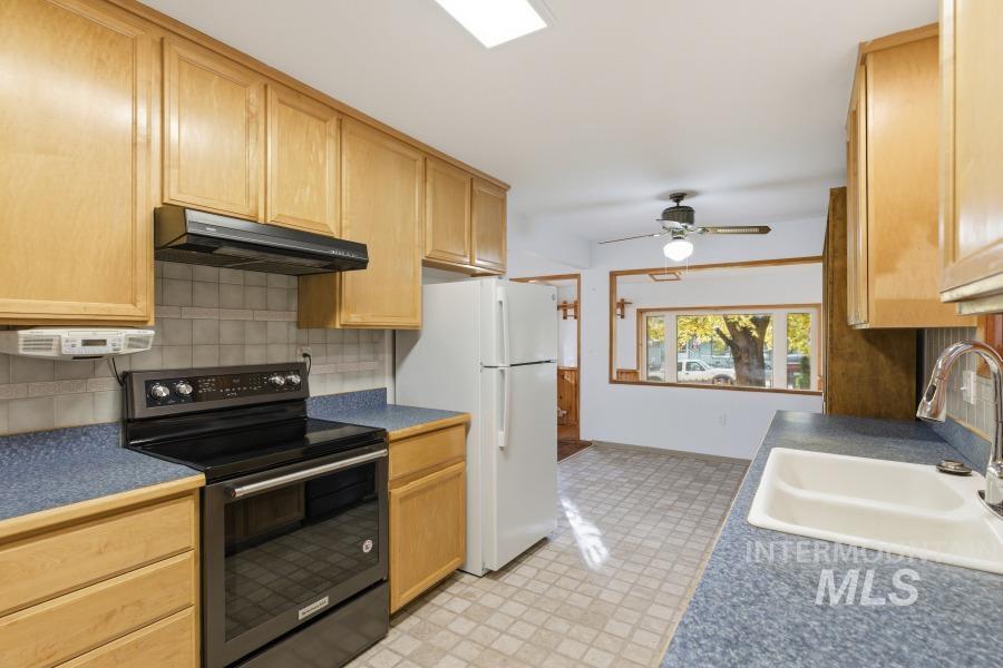 Kitchen featuring tasteful backsplash, black range with electric stovetop, under cabinet range hood, freestanding refrigerator, and a ceiling fan