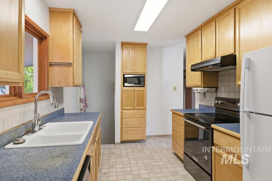Kitchen with black appliances, decorative backsplash, light brown cabinetry, and dark countertops