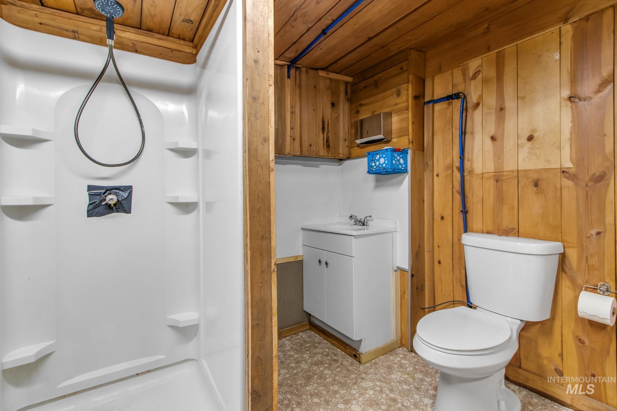 Full bathroom with wooden walls, a stall shower, vanity, and wood ceiling