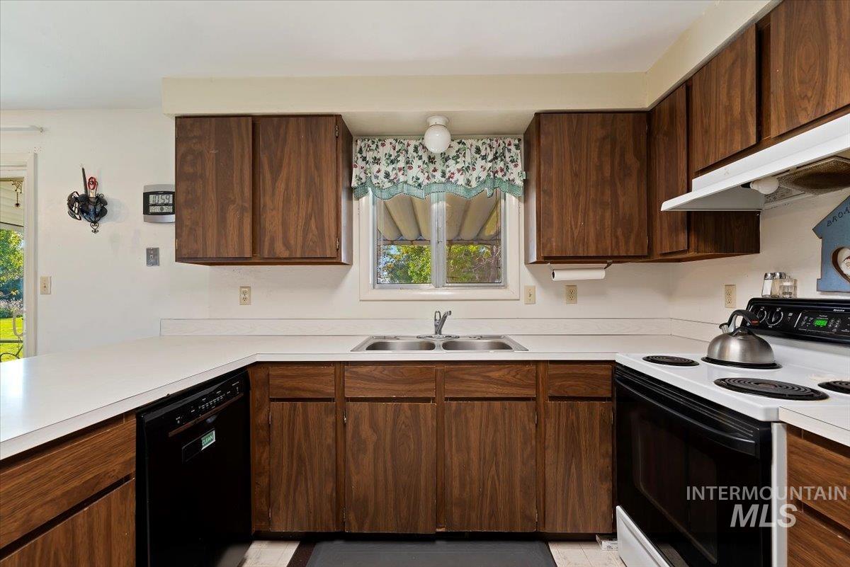Kitchen with electric range oven, dishwasher, light countertops, under cabinet range hood, and dark brown cabinets