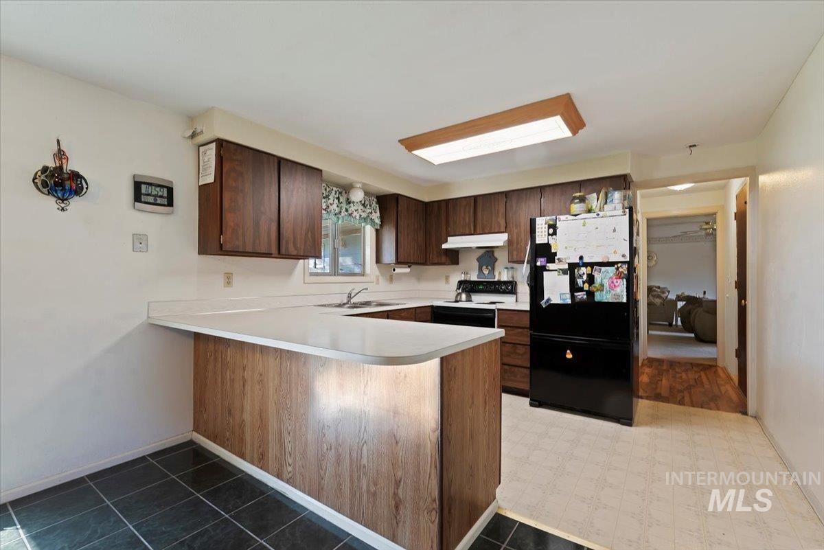 Kitchen with freestanding refrigerator, light countertops, a peninsula, electric range oven, and dark brown cabinets