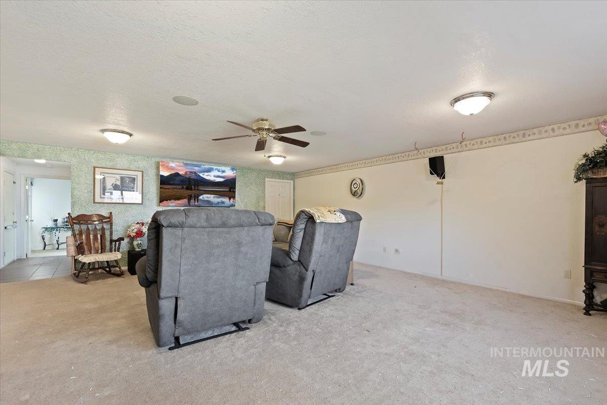 Living area featuring a textured ceiling, light colored carpet, and ceiling fan