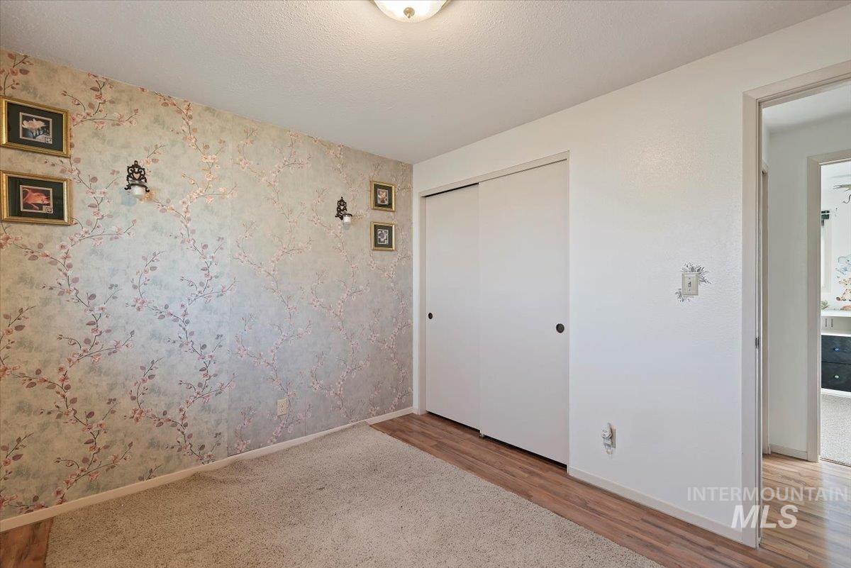 Unfurnished bedroom with wood finished floors, wallpapered walls, a textured ceiling, and a closet