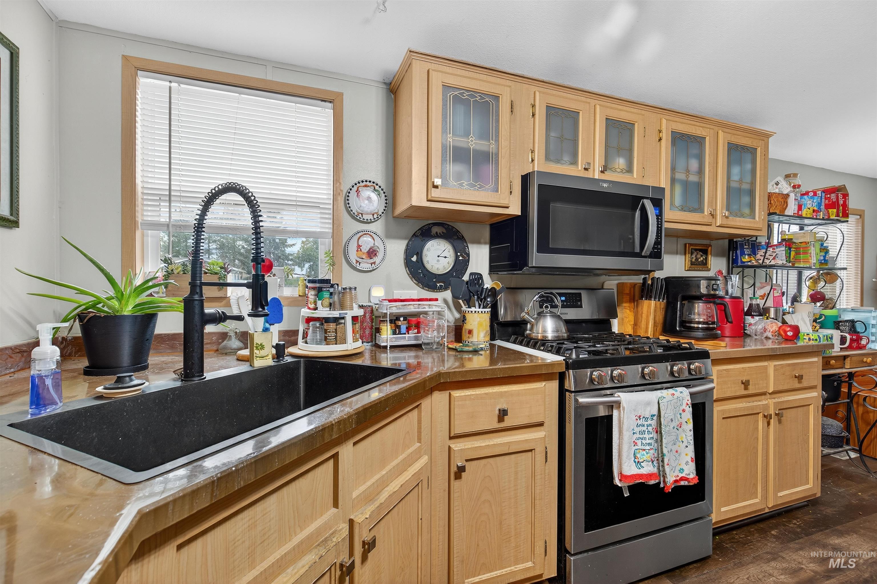 Kitchen featuring stainless steel appliances, light brown cabinetry, glass insert cabinets, and dark wood-style floors