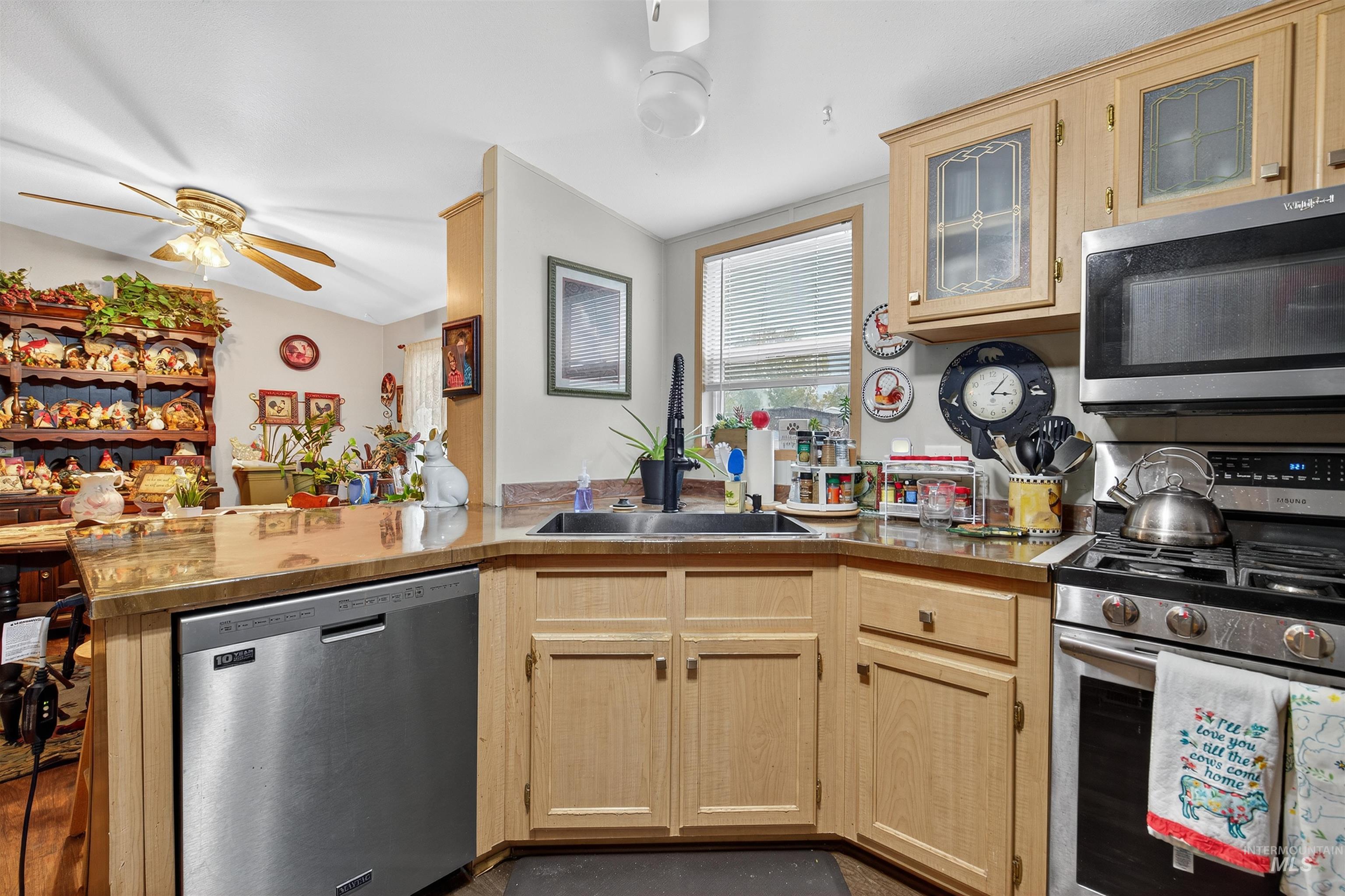Kitchen featuring appliances with stainless steel finishes, light brown cabinets, glass insert cabinets, a peninsula, and light countertops