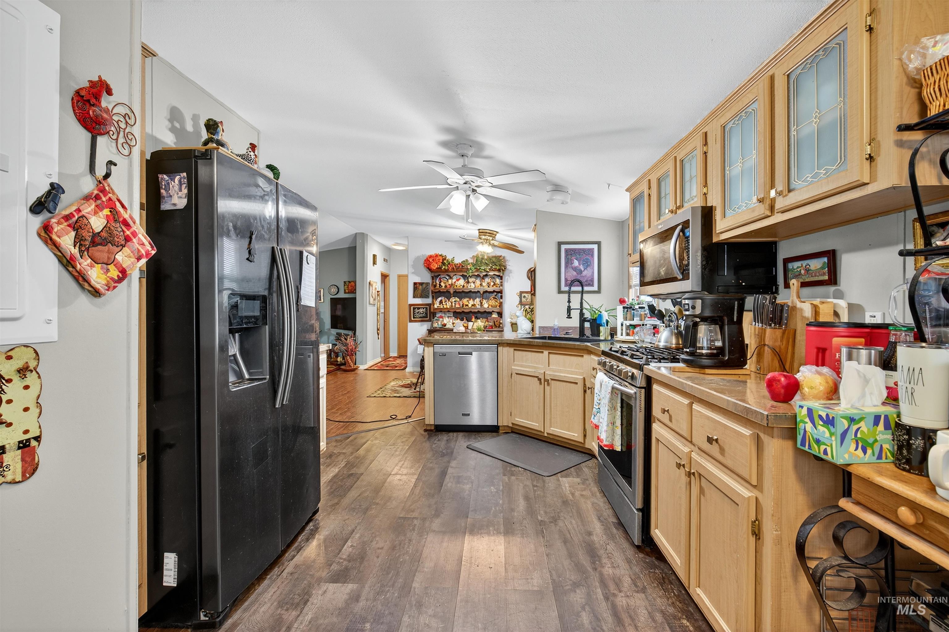 Kitchen with a peninsula, appliances with stainless steel finishes, light brown cabinetry, dark wood finished floors, and glass insert cabinets