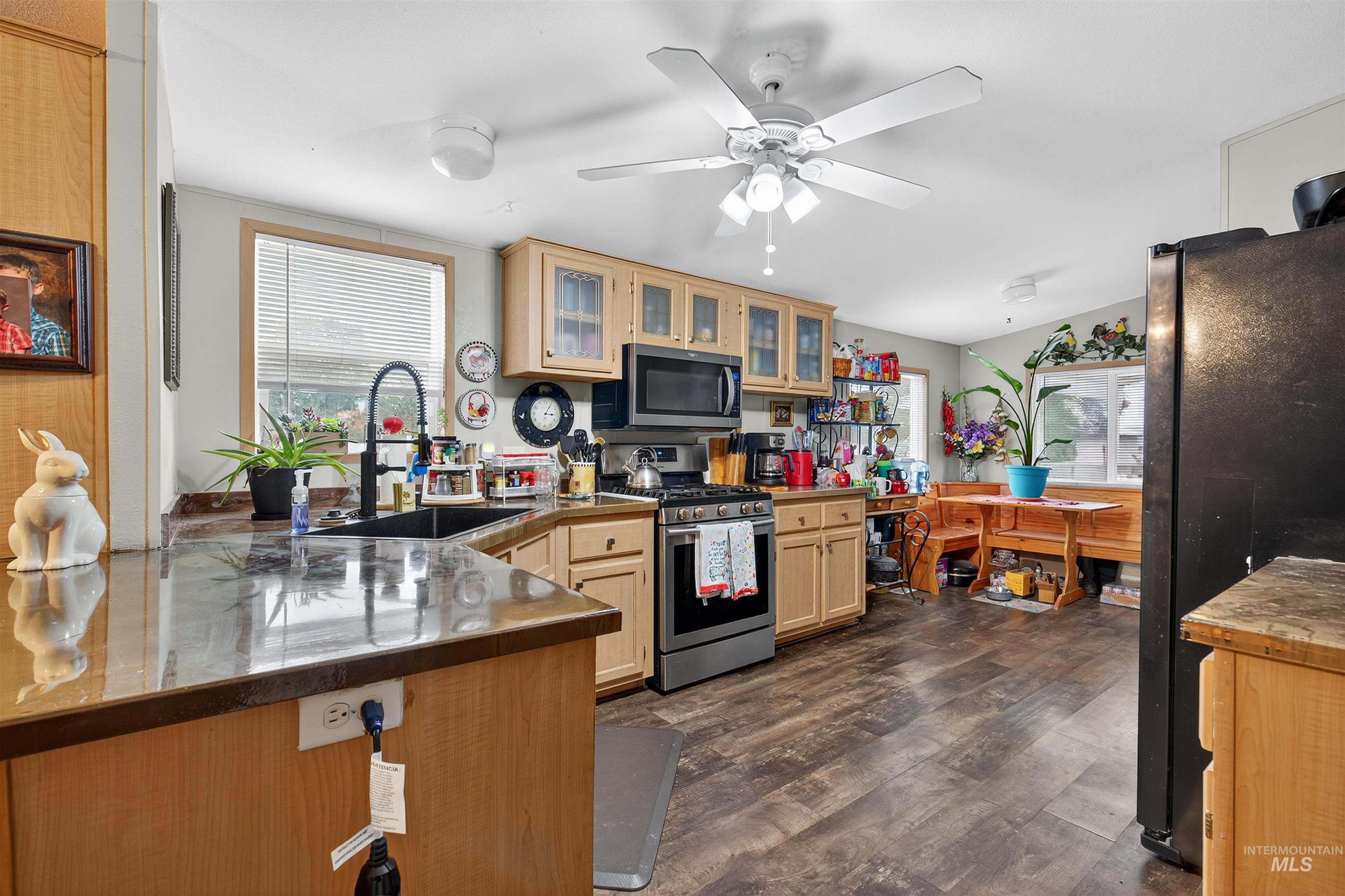 Kitchen featuring glass insert cabinets, appliances with stainless steel finishes, dark wood-type flooring, light brown cabinets, and a peninsula