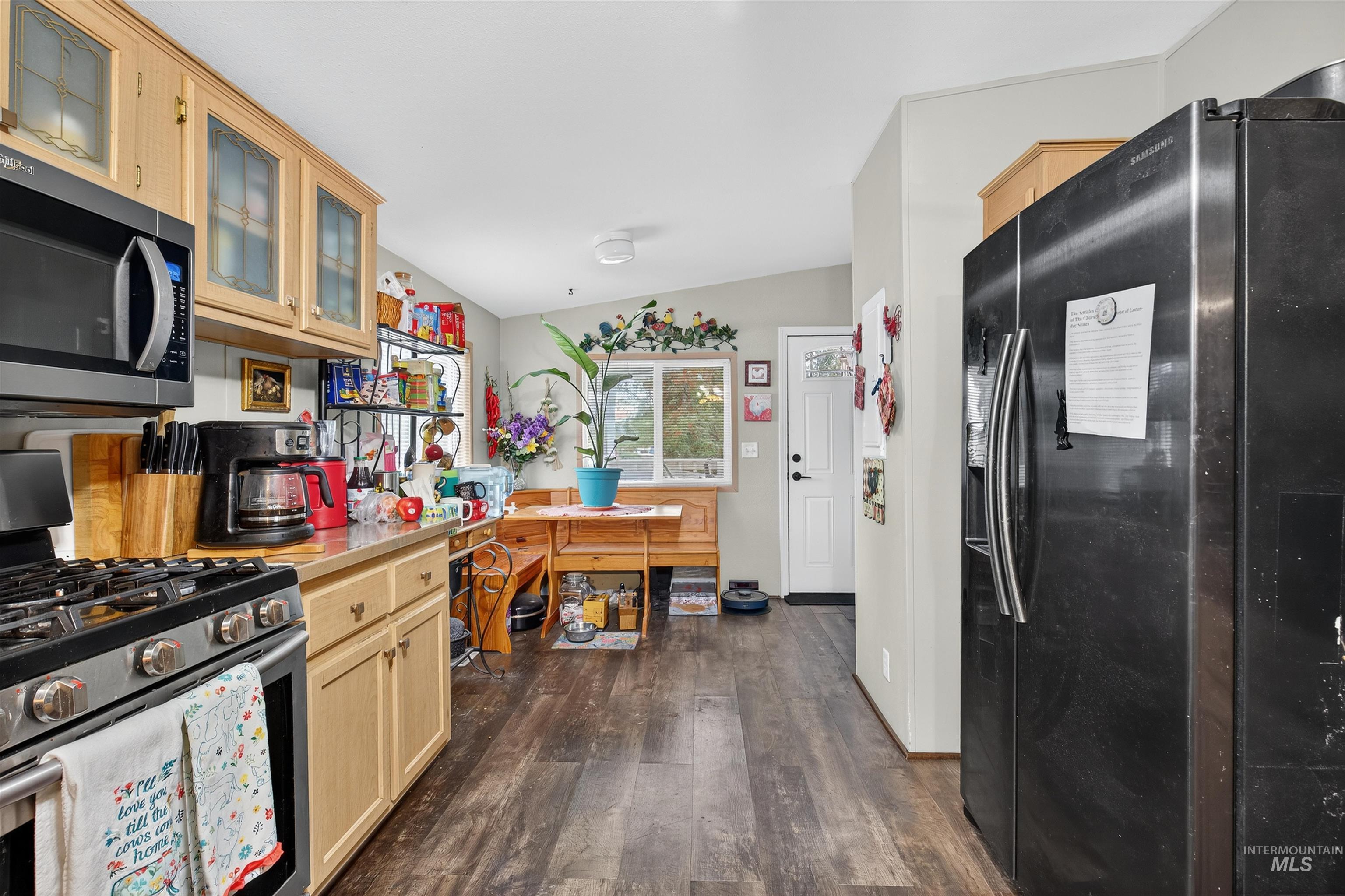Kitchen with appliances with stainless steel finishes, light countertops, dark wood-style flooring, glass insert cabinets, and vaulted ceiling