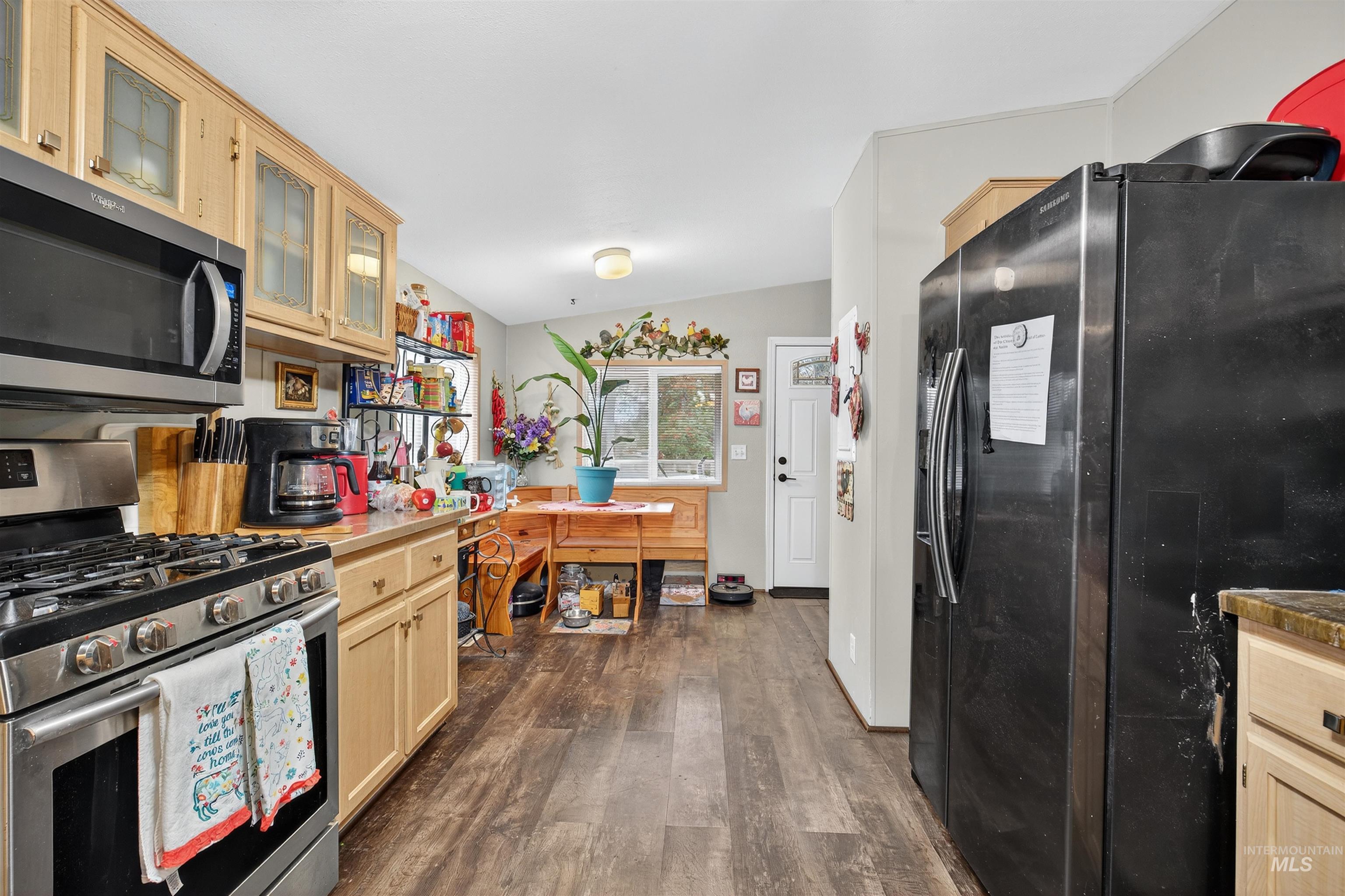 Kitchen featuring appliances with stainless steel finishes, glass insert cabinets, dark wood-style floors, lofted ceiling, and light brown cabinetry