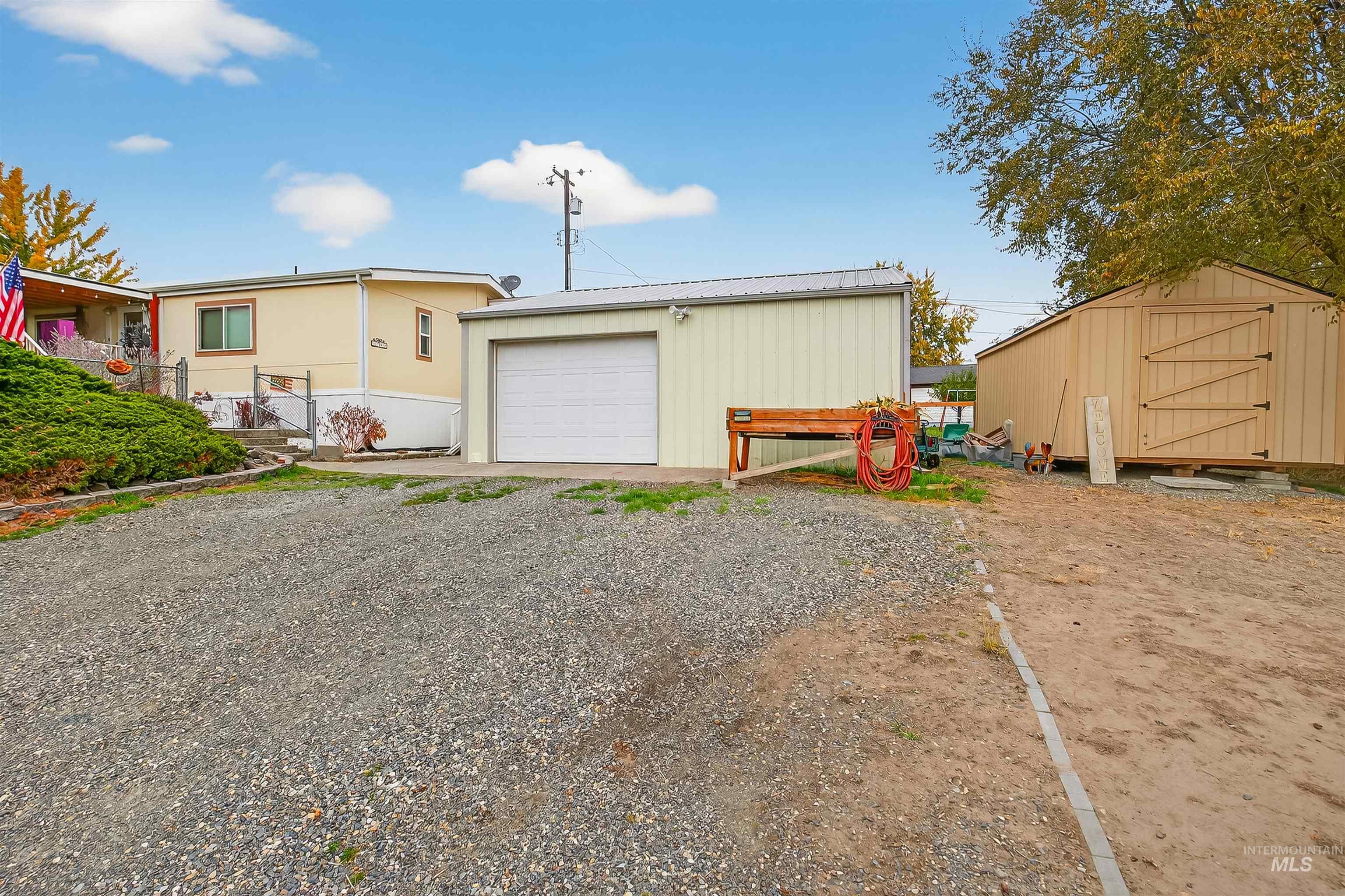 View of front facade with an outdoor structure, a garage, a metal roof, and gravel driveway