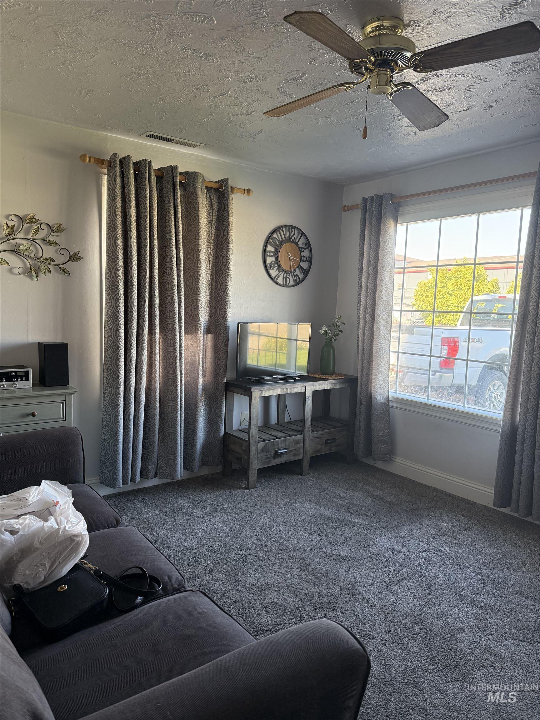 Living room featuring a textured ceiling, carpet floors, and a ceiling fan