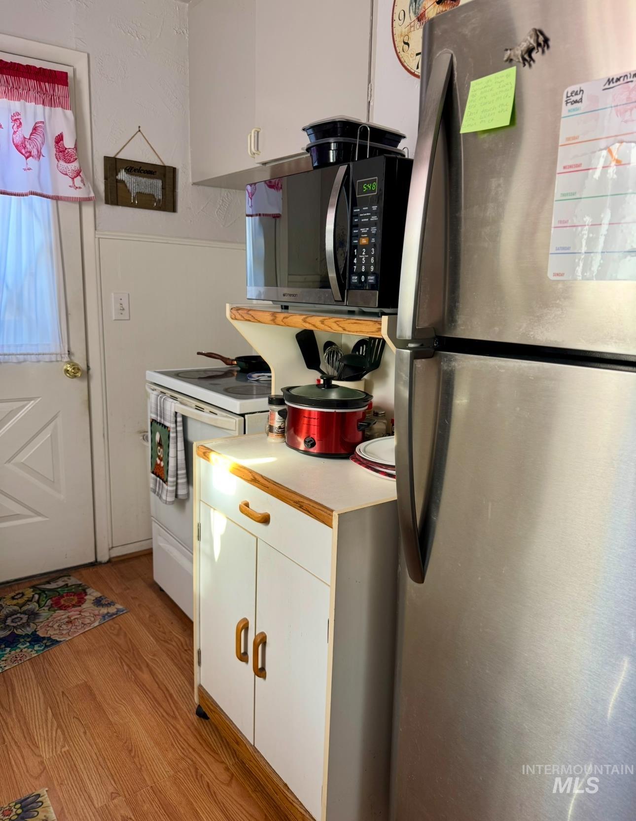 Kitchen with appliances with stainless steel finishes, light wood finished floors, light countertops, white cabinetry, and a textured wall
