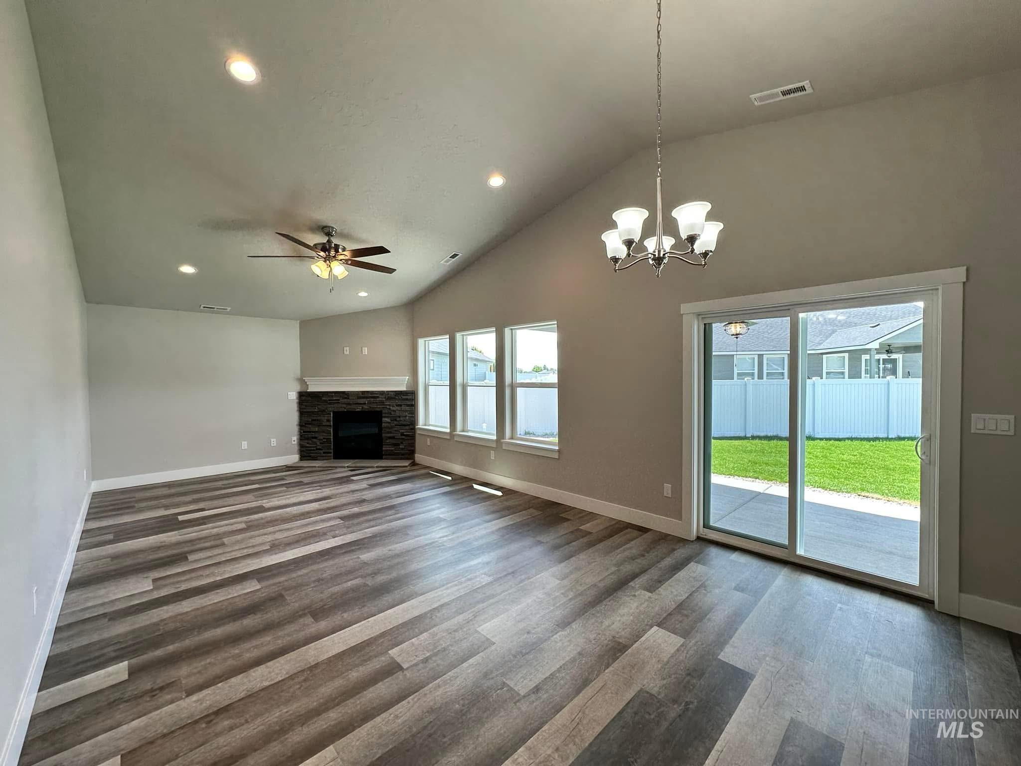 Unfurnished living room featuring high vaulted ceiling, a stone fireplace, dark wood finished floors, a chandelier, and recessed lighting