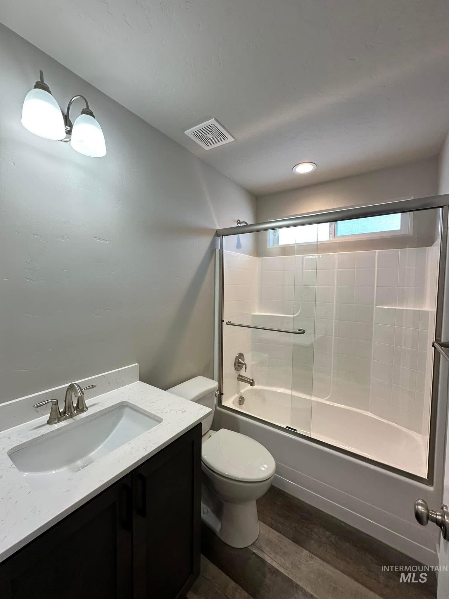 Bathroom with dark wood-style flooring, shower / bath combination with glass door, and vanity