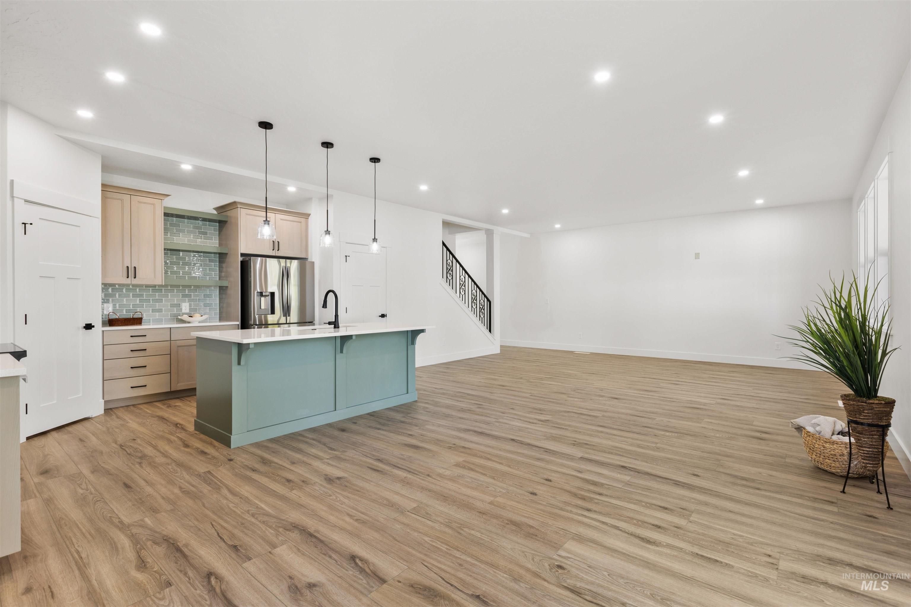 Kitchen featuring hanging light fixtures, an island with sink, open floor plan, light wood-type flooring, and a kitchen breakfast bar