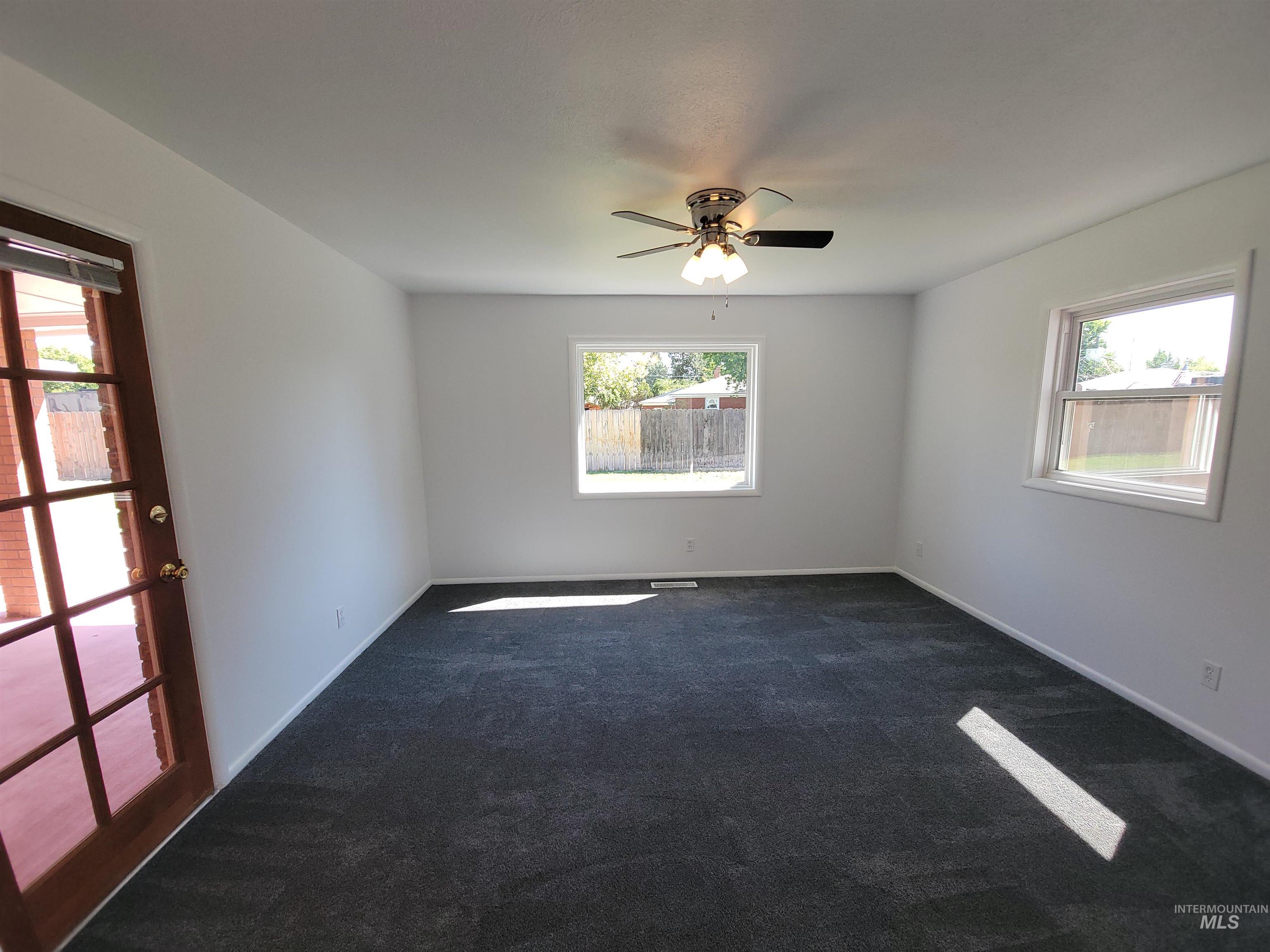 Spare room with plenty of natural light, dark carpet, and a ceiling fan