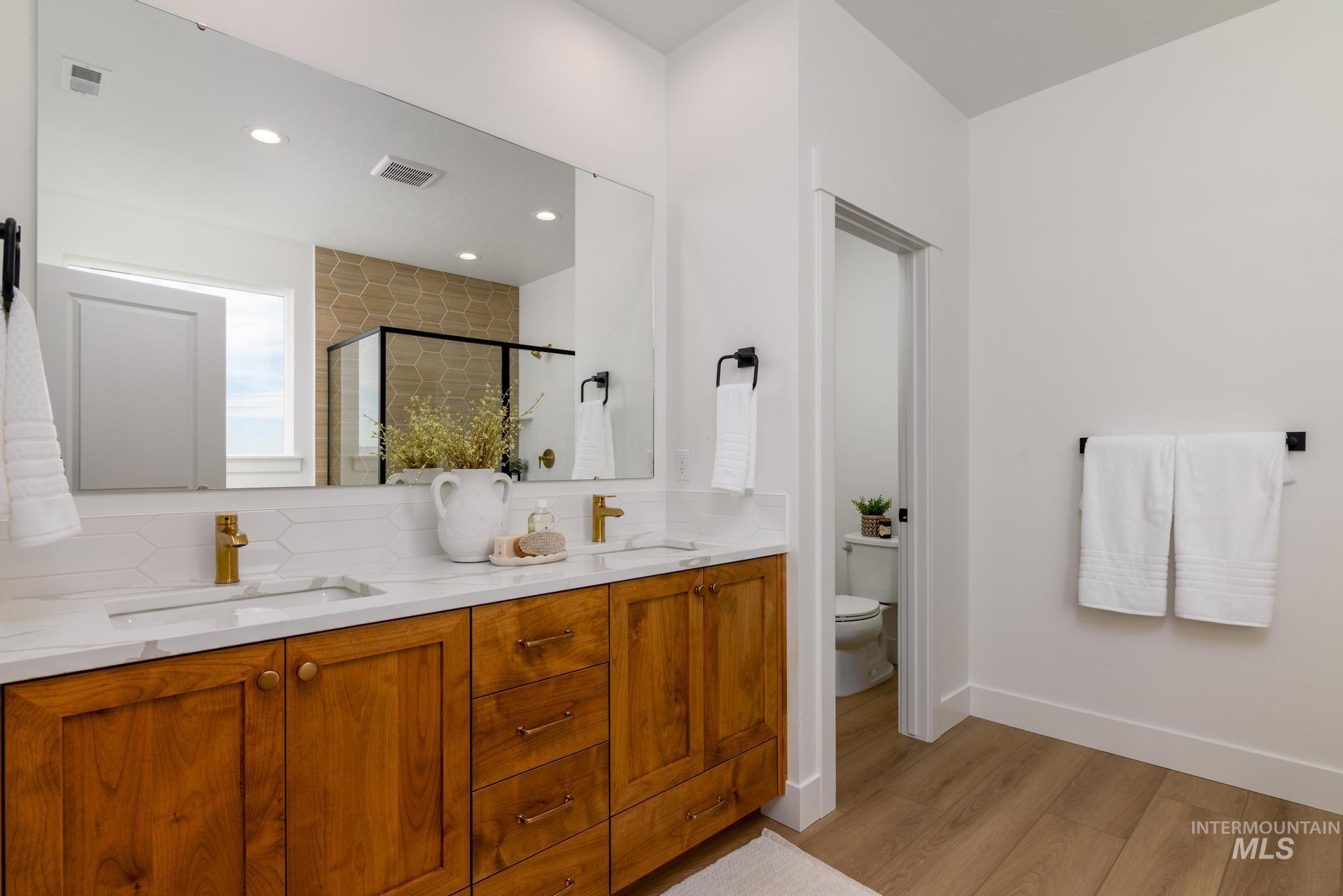 Bathroom with a stall shower, light wood-style floors, double vanity, backsplash, and recessed lighting