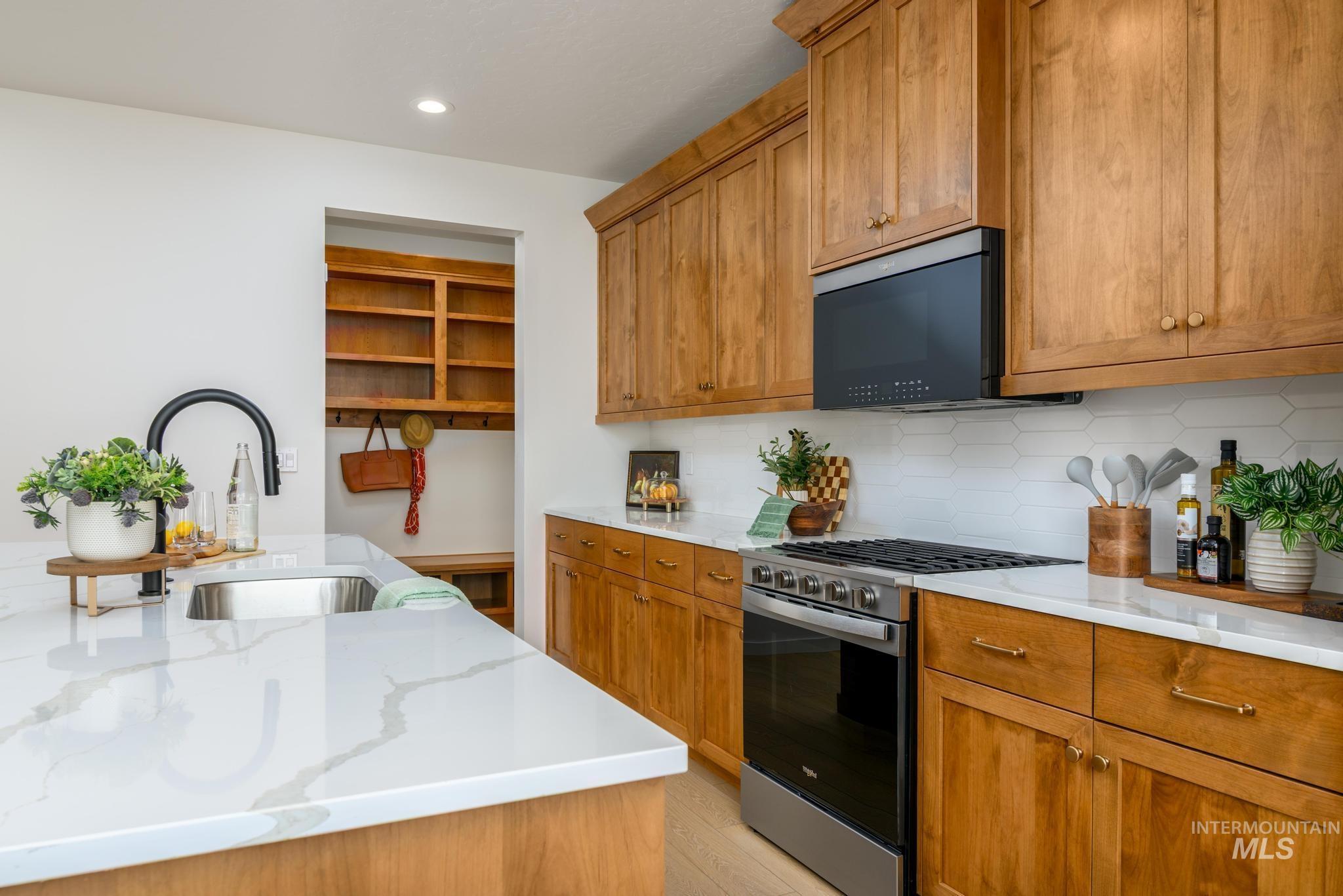 Kitchen featuring stainless steel range with gas stovetop, brown cabinetry, decorative backsplash, black microwave, and recessed lighting