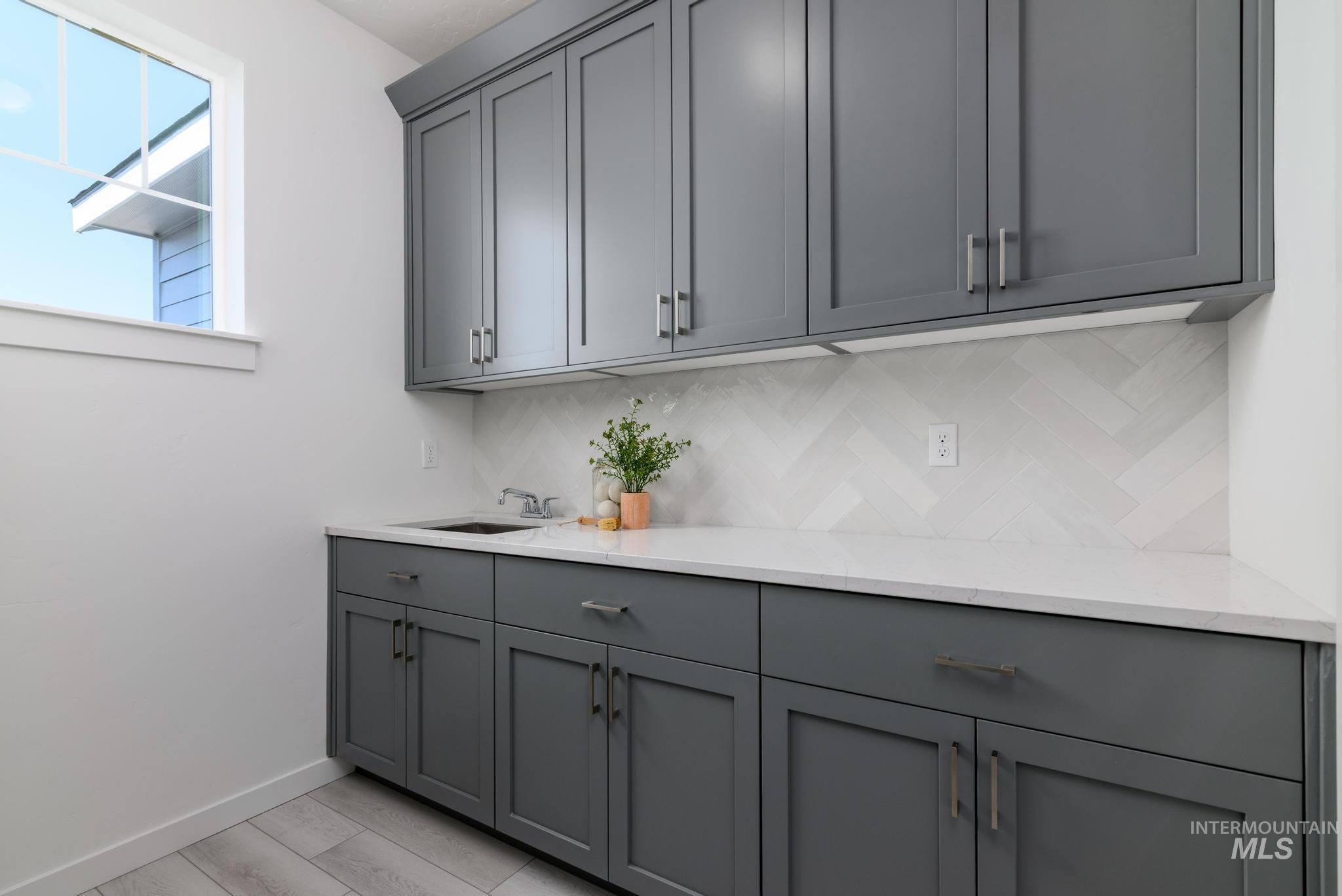 Bar area with gray cabinetry, backsplash, light stone counters, and light wood-style floors