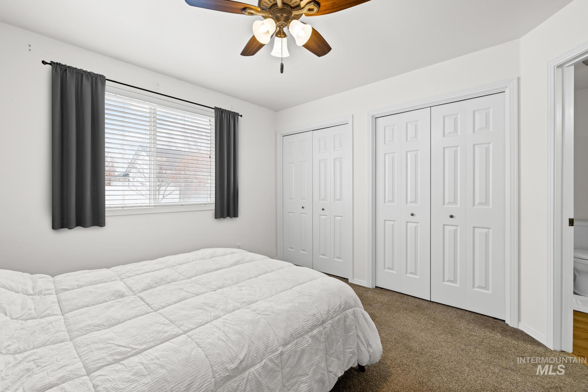 Bedroom with two closets, dark colored carpet, and ceiling fan