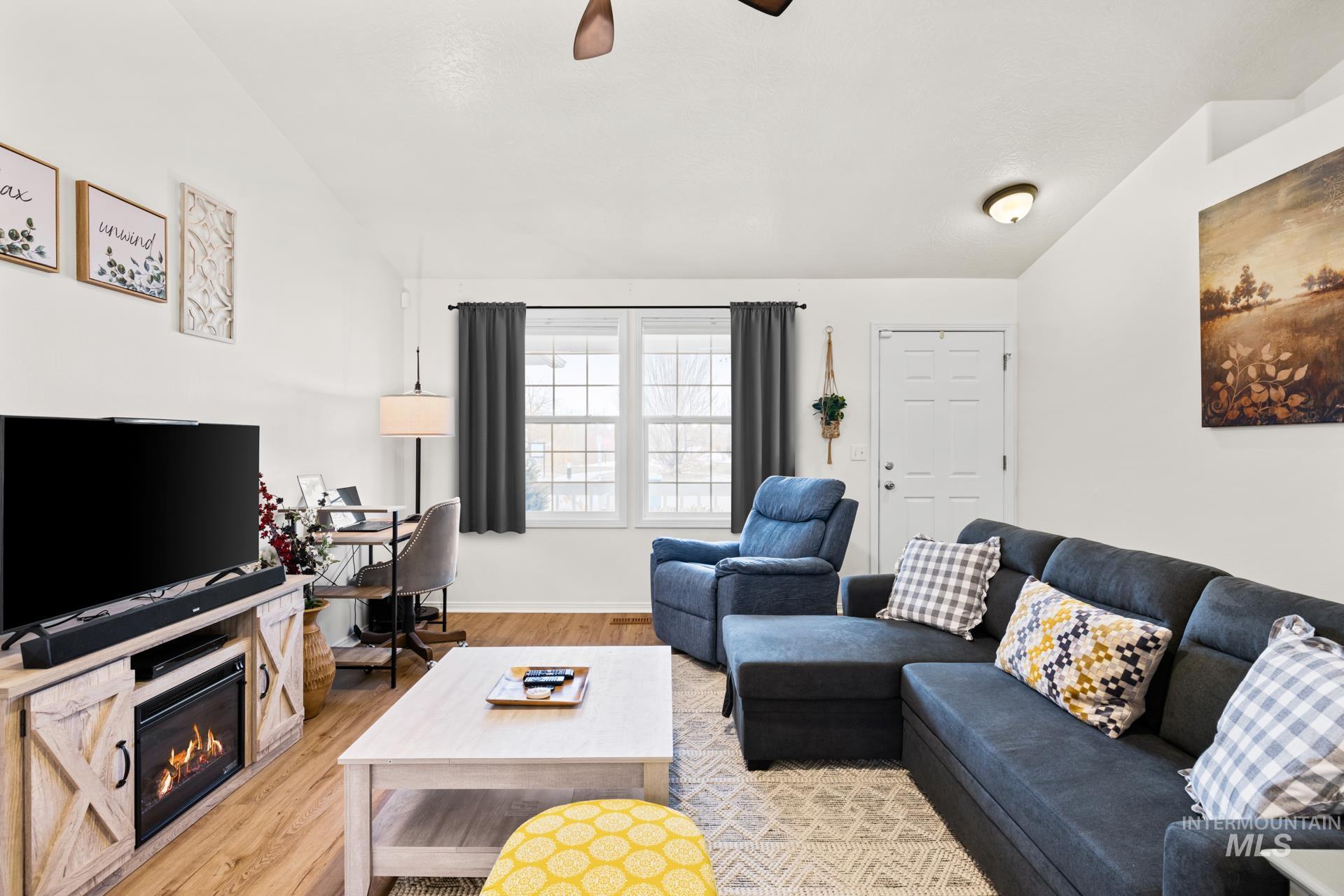 Living room featuring light wood-style flooring, a glass covered fireplace, lofted ceiling, and ceiling fan