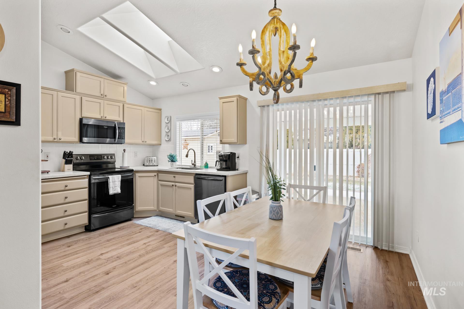 Kitchen featuring a skylight, lofted ceiling, light countertops, black appliances, and light wood-style floors