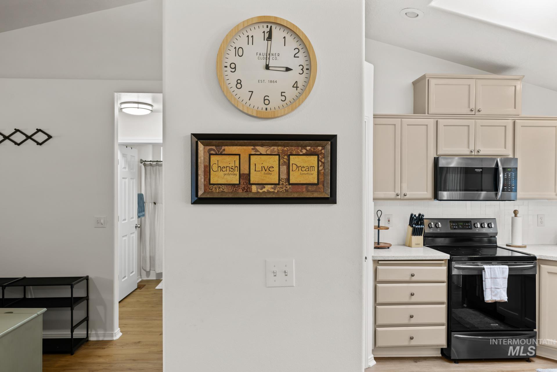 Kitchen with vaulted ceiling, black electric range oven, light wood finished floors, cream cabinets, and backsplash