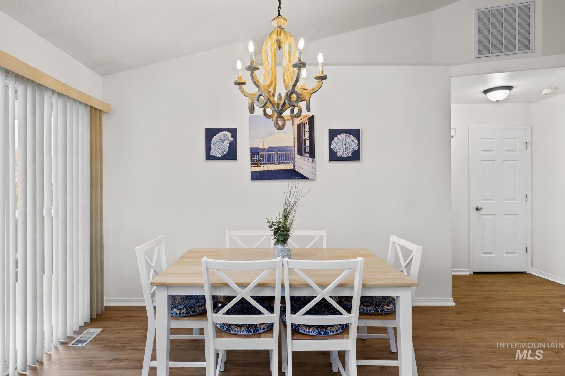 Dining space with wood finished floors, vaulted ceiling, and a chandelier