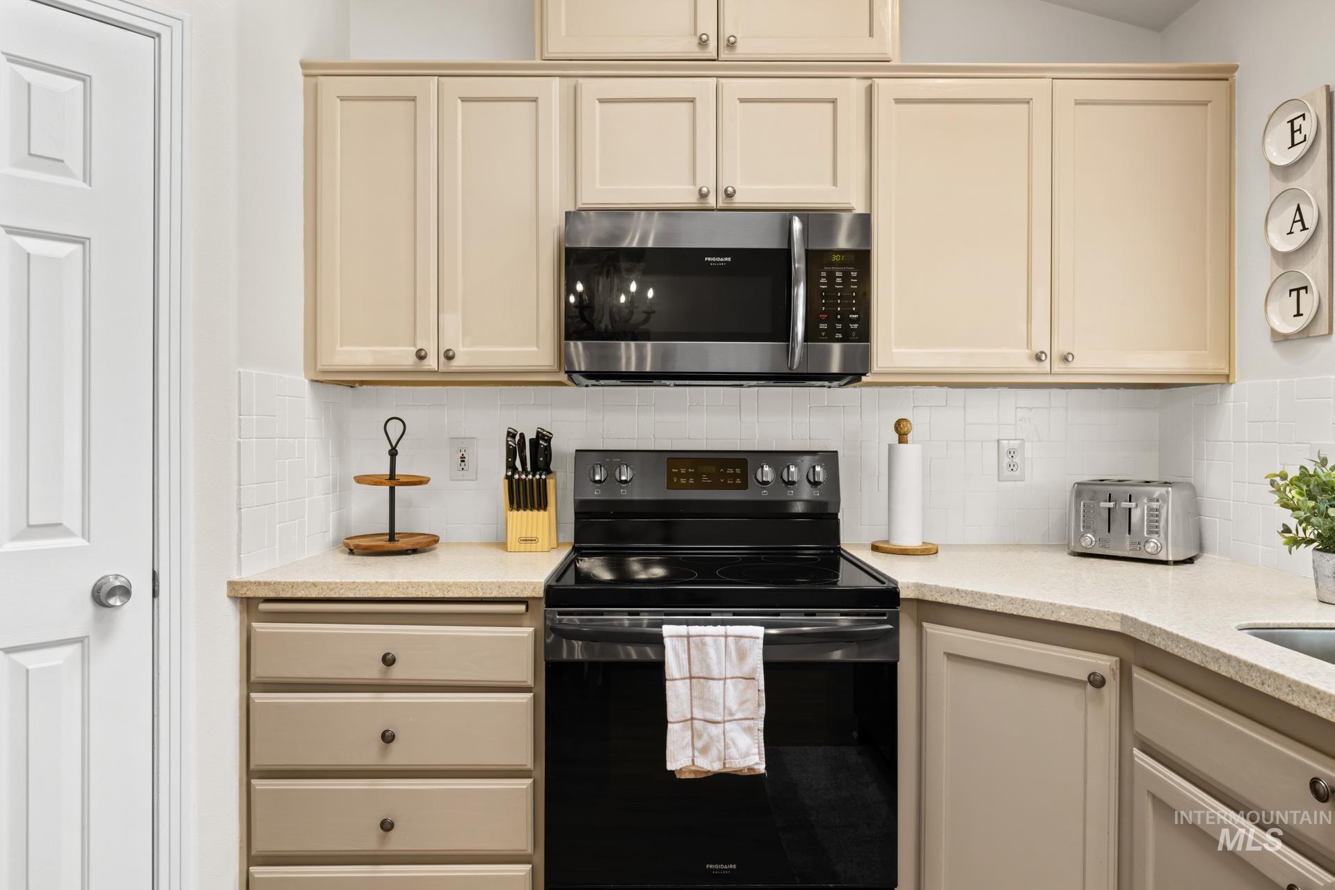 Kitchen with electric range, cream cabinetry, and tasteful backsplash