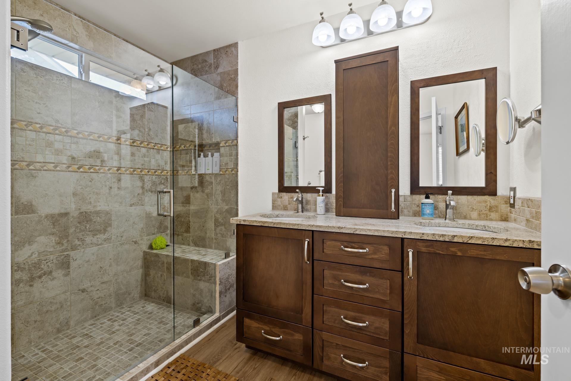 Bathroom featuring double vanity, a shower stall, and wood finished floors