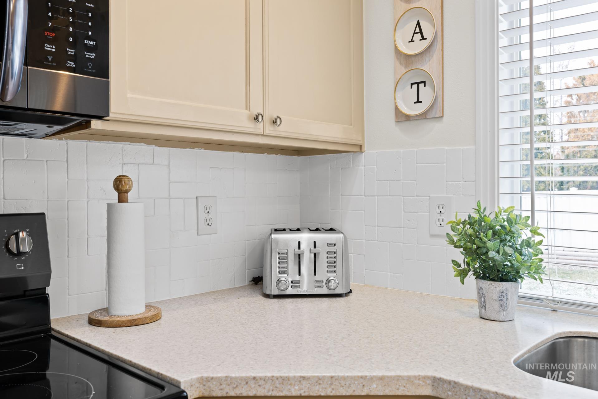Kitchen view of electric range, stainless steel microwave, light stone countertops, and backsplash